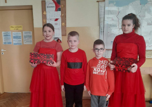 Dwie dziewczynki i dwóch chłopców stoi w szkolnej sali, są ubrani na czerwono.